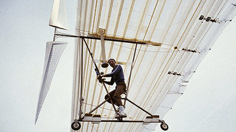 Ian Parker pictured flying n a human-powered aircraft. The wings of the aircraft span across the image.